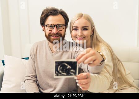 Glückliches kaukasisches Ehepaar, das ein Ultraschallbild der Schwangerschaft ihres ungeborenen Babys zeigt. . Hochwertige Fotos Stockfoto