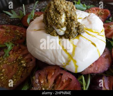 Köstlicher Burrata-Salat mit Tomaten, Rucola und Pesto-Sauce Stockfoto