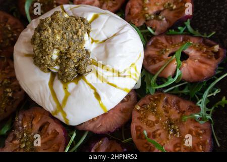 Cenital-Bild einer Buratta Mozzarella mit Pesto-Sauce und Tomaten Stockfoto