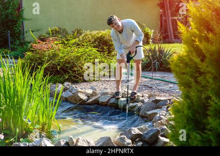Der Mensch reinigt den Boden des Gartenteichs mit dem Hochdruckreiniger von Schlamm und Schlamm. Stockfoto