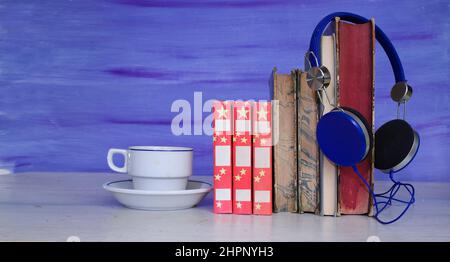 Hörbuch-Konzept mit Bücherstapel, Vintage-Kopfhörern und einer Tasse Kaffee. Podcasting, Bildung, digitales Buchkonzept. Stockfoto