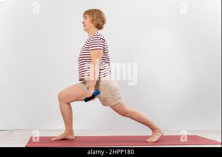 Ältere Frau macht Ausfallschritte auf weißem Hintergrund. Stockfoto