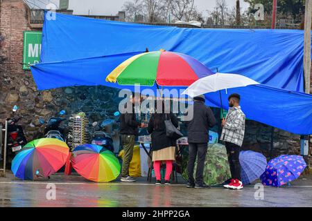 Srinagar, Indien. 22nd. Februar 2022. Indische Touristen kaufen Regenschirme von einem Straßenhändler bei Niederschlägen in Srinagar. Der obere Teil des Kaschmir-Tals erhielt Schneefall, selbst als die Ebenen von Regenfällen überfallen wurden. Der Wettermann prognostizierte in den nächsten 24 Stunden weit verbreitete leichte bis mäßige Regenfälle sowie Schnee über Jammu und Kaschmir. Kredit: SOPA Images Limited/Alamy Live Nachrichten Stockfoto