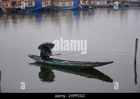 Srinagar, Indien. 22nd. Februar 2022. Ein Bootsmann hält einen Regenschirm, während er sein Boot während der Regenfälle in Srinagar über den Dal-See rudert. Der obere Teil des Kaschmir-Tals erhielt Schneefall, selbst als die Ebenen von Regenfällen überfallen wurden. Der Wettermann prognostizierte in den nächsten 24 Stunden weit verbreitete leichte bis mäßige Regenfälle sowie Schnee über Jammu und Kaschmir. Kredit: SOPA Images Limited/Alamy Live Nachrichten Stockfoto