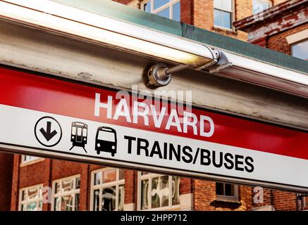 Cambridge, Massachusetts, USA - 16. Februar 2022: Nahaufnahme des Schildes für die U-Bahn- und Bushaltestelle der MBTA Red Line am Harvard Square. Gebäude am Harvard Square Stockfoto