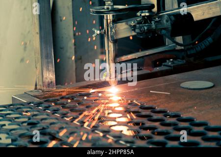 Plasmaschneidemaschine brennt durch ein dickes Stahlblech, indem sie Tropfen geschmolzenem Metall in verschiedene Richtungen streut Stockfoto