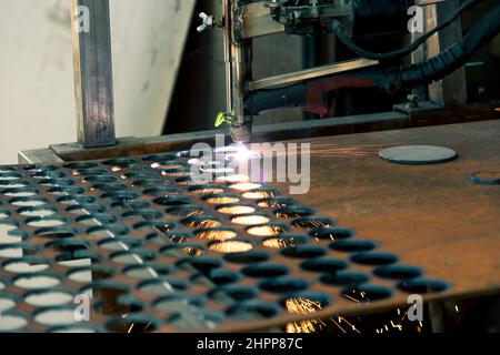 Plasmaschneidemaschine brennt durch ein dickes Stahlblech, indem sie Tropfen geschmolzenem Metall in verschiedene Richtungen streut Stockfoto