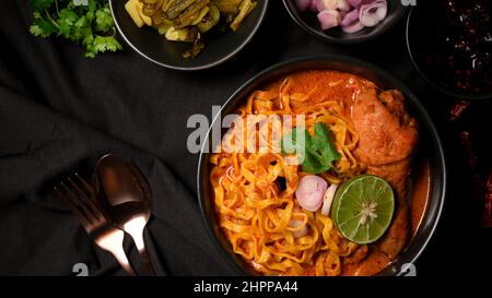Khao Soi Kai, Northern Thai-Nudeln mit Hähnchendrumstick serviert mit eingelegtem Senfgrün, Schalotten, Limette. Besteck auf schwarzem Tisch. Top vi Stockfoto