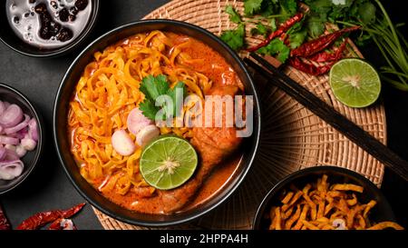 Draufsicht, Khao Soi Kai, cremig-würzige gelbe Kerrsuppe mit Hühnerdrumstick, serviert mit asiatischer Beilage. Nordthailändisches Speisekonzept Stockfoto