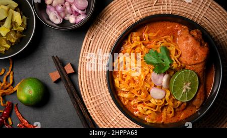 Leckere Suppe aus nordthailändischen, gelben Kokosnussnudeln mit Hühnchen. Khao Soi Kai in einer Schüssel mit Limette, Schalotten und Koriander. Stockfoto