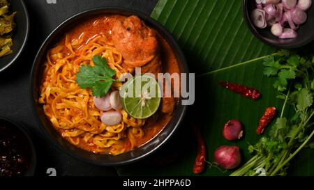 Draufsicht, Khao Soi Kai Schale über grünem Bananenblatt Hintergrund mit Gemüse Beilage. Nordthailändisches Speisekonzept. Stockfoto