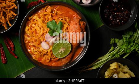 Draufsicht auf einen leckeren Khao Soi Kai in einer schwarzen Schüssel mit frischem Gemüse auf Bananenblatt Hintergrund. Nordthailändisches Speisekonzept. Stockfoto