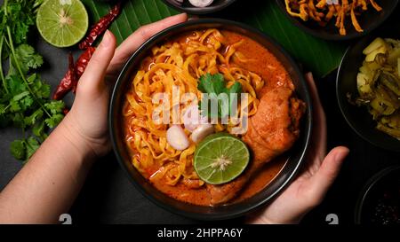 Draufsicht, Frau, die eine Khao Soi Kai Schale serviert. Köstliches Konzept der nordthailändischen Küche. Nudeln, eine Pudelsuppe mit Hühnchen. Stockfoto