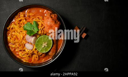 Overhead Shot, Khao Soi Kai oder Hühnerfleisch-Kerri mit Gewürzen und Eiernudeln auf schwarzem Hintergrund. Nordthailändisches Speisekonzept Stockfoto