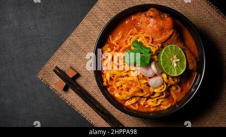Blick von oben auf den Khao Soi Kai oder die Nudeln mit einer Pudersuppe mit Hühnchen. Konzept der nordthailändischen Küche. Stockfoto