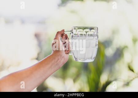 Hand hält Zitronenwasser oder Limonade in Bier stein Glas vor sonnigen Hinterhof Bokeh, Konzept der Sommerentspannung und Getränke Stockfoto