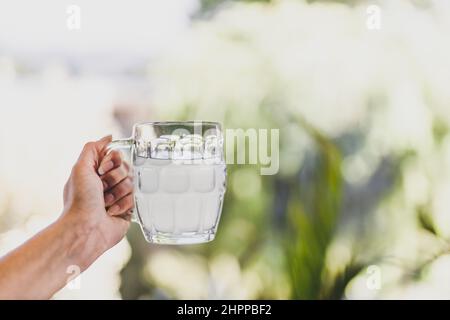Hand hält Zitronenwasser oder Limonade in Bier stein Glas vor sonnigen Hinterhof Bokeh, Konzept der Sommerentspannung und Getränke Stockfoto