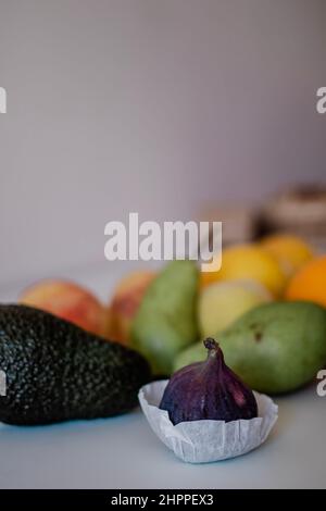 Frische Feige im Vordergrund mit anderen Früchten auf hellem Hintergrund auf dem Tisch Stockfoto