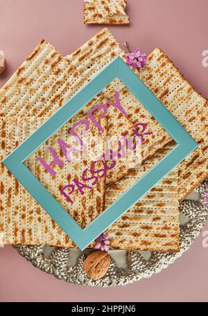 Pesach Feiertagskonzept - jüdischer Feiertag Pesach. Matzah auf traditionellem Seder-Teller mit einer Flasche Rotwein, Nüssen auf purpurem Hintergrund und Blau Stockfoto