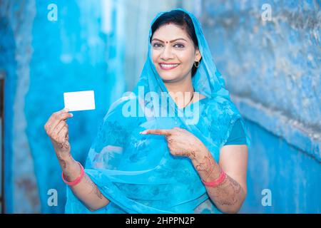 Traditionelle indische Frau zeigt weißen Debit-Kreditkarte Mockup, glücklich Frau trägt Sari zeigen hält leere Geschäft oder elektronische Ca Stockfoto