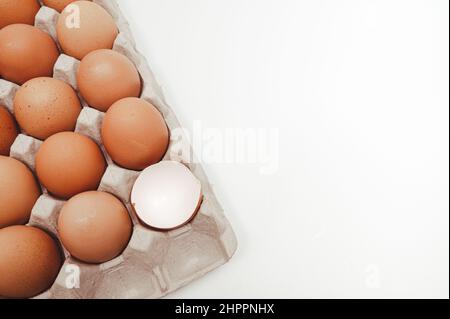 Weißer Hintergrund mit Kopierplatz, Eiern in einem Papierfach und gebrochenen Eierschalen. Stockfoto