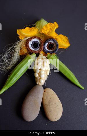 Lustige Gesicht aus Lebensmitteln, landwirtschaftliche Produkte aus Dachgarten, kleinen Mais, Kürbisblume, Maisseide, Okra Obst, Kies und Augen häkeln aus Stockfoto