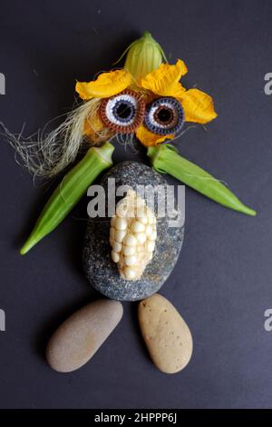 Lustige Gesicht aus Lebensmitteln, landwirtschaftliche Produkte aus Dachgarten, kleinen Mais, Kürbisblume, Maisseide, Okra Obst, Kies und Augen häkeln aus Stockfoto