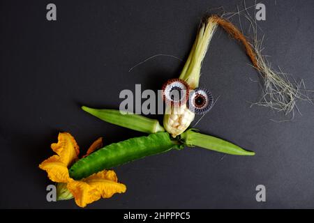 Lustige Gesicht aus Lebensmitteln, landwirtschaftliche Produkte aus Dachgarten, kleinen Mais, Kürbisblume, Maisseide, Okra Obst, Kies und Augen häkeln aus Stockfoto