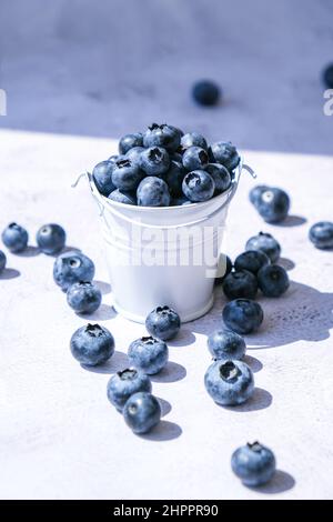 Heidelbeeren in einem kleinen Eimer auf Betongrund. Gesunde Bio saisonalen Obst Hintergrund. Bio-Lebensmittel. Gesunder Sommersnack. Speicherplatz kopieren Stockfoto