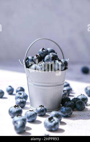 Heidelbeeren in einem kleinen Eimer auf Betongrund. Gesunde Bio saisonalen Obst Hintergrund. Bio-Lebensmittel. Gesunder Sommersnack. Speicherplatz kopieren Stockfoto