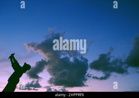 Lustige Szene bei Sonnenuntergang, wenn die Silhouette einer vietnamesischen Frau läuft, wenn die Tierform von der Wolkenjagd kommt, stellt sich die Frau auf dem Dach auf, wenn sie zu Hause in Gesellschaft bleibt Stockfoto