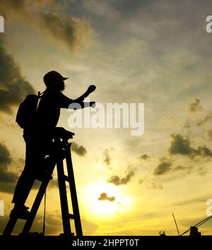 Erstaunliche Szene von vietnamesischen Frau, wenn zu Hause bleiben durch soziale Distanzierung, sie machen Spaß beim Sonnenuntergang auf dem Dach durch Stand auf Leiter, wenn die Sonne auf m untergehen Stockfoto