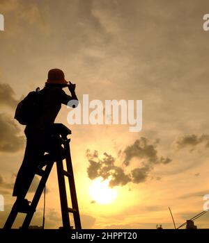 Erstaunliche Szene von vietnamesischen Frau, wenn zu Hause bleiben durch soziale Distanzierung, sie machen Spaß beim Sonnenuntergang auf dem Dach durch Stand auf Leiter, wenn die Sonne auf m untergehen Stockfoto