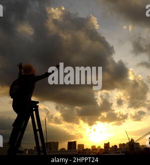 Erstaunliche Szene von vietnamesischen Frau, wenn zu Hause bleiben durch soziale Distanzierung, sie machen Spaß beim Sonnenuntergang auf dem Dach durch Stand auf Leiter, wenn die Sonne auf m untergehen Stockfoto