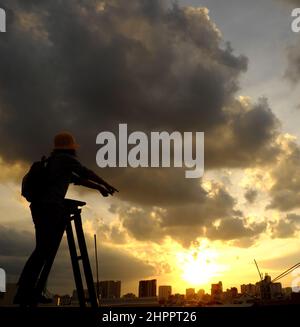 Erstaunliche Szene von vietnamesischen Frau, wenn zu Hause bleiben durch soziale Distanzierung, sie machen Spaß beim Sonnenuntergang auf dem Dach durch Stand auf Leiter, wenn die Sonne auf m untergehen Stockfoto