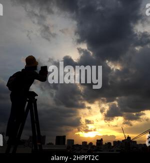 Erstaunliche Szene von vietnamesischen Frau, wenn zu Hause bleiben durch soziale Distanzierung, sie machen Spaß beim Sonnenuntergang auf dem Dach durch Stand auf Leiter, wenn die Sonne auf m untergehen Stockfoto