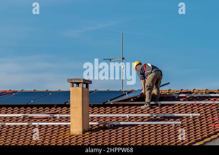 Ein Techniker legt die Sonnenkollektoren einer Photovoltaikanlage auf ein rot gefliestes Dach Stockfoto