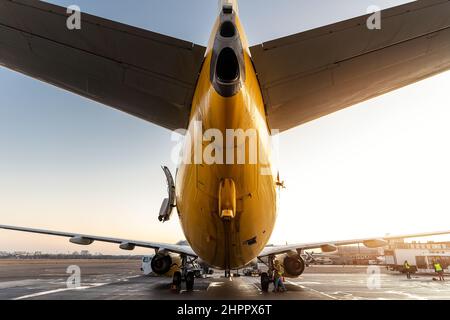 Landschaftlich schöne, schräge pov-Rückansicht von hinten nach unten eines großen modernen Passagierflugzeuges auf dem Parkplatz am Boden vor dem Hintergrund des blau-orangenen Sonnenuntergangs am Sonnenaufgangshimmel Stockfoto