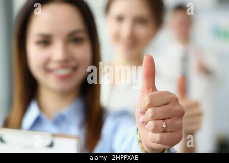 Lächelnde Frau zeigt Daumen nach oben und bestätigt den Erfolg an der Kamera Stockfoto
