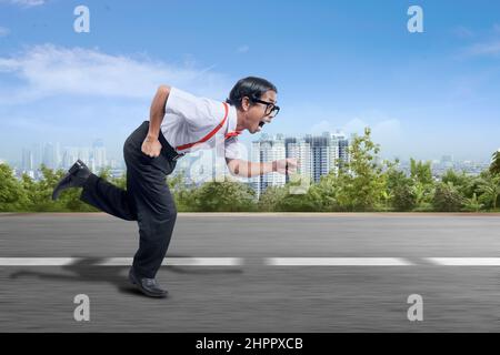 Asiatischer Nerd mit hässlichem Gesicht, das auf der Straße mit Stadtansichten im Hintergrund läuft Stockfoto
