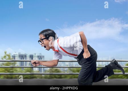 Asiatischer Nerd mit hässlichem Gesicht, das auf der Straße mit Stadtansichten im Hintergrund läuft Stockfoto