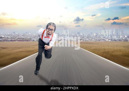 Asiatischer Nerd mit hässlichem Gesicht, das auf der Straße mit Stadtansichten im Hintergrund läuft Stockfoto