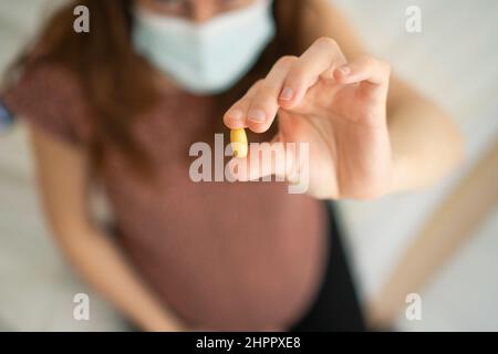Nahaufnahme der Pille in der Hand. Im Hintergrund ist eine Schwangerin. Einnahme von Vitaminen während der Schwangerschaft. Medizinische Versorgung und Medikamente während der Schwangerschaft und der Geburt. Stockfoto