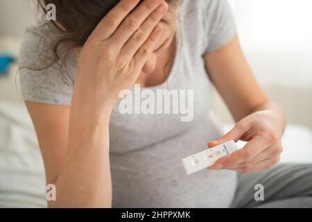 Schwanger Frau macht Test. Nahaufnahme der Finger, die den Express-Antigen-Covid-Corona-Test halten, positives Ergebnis sarscov2. Stockfoto