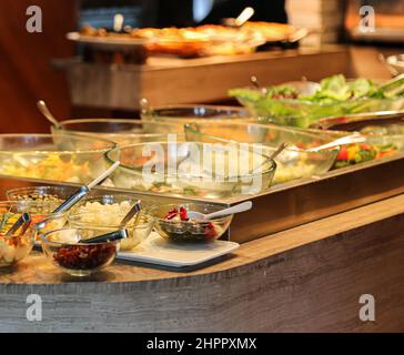 Salat und Obst in Glasschüsseln auf Eis und Caprese-Salat auf weißem Teller mit Edelstahlzangen an der kalten Salatbar am Buffet Stockfoto