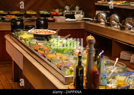 Salat und Obst in Glasschüsseln auf Eis und Caprese-Salat auf weißem Teller mit Edelstahlzangen an der kalten Salatbar am Buffet Stockfoto