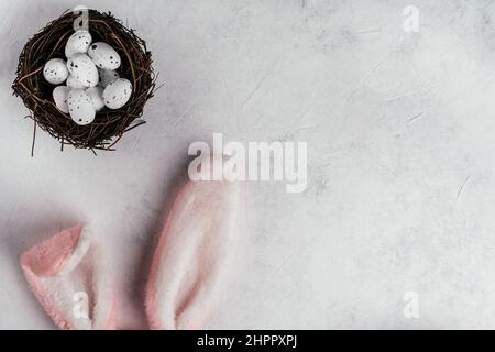 Ostern Komposition aus weißen Fleck Wachteleiern in braunem Nest auf weiß grauem Papierhintergrund und Ausschneiden rosa Hase Kaninchen Spielzeug flauschige Haarohren. Sehr, Sehr Stockfoto