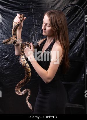 Foto einer Frau mit Schlangen in den Händen auf dunklem Hintergrund Stockfoto