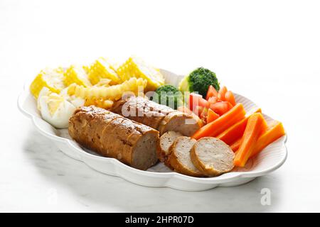 Hackbraten mit Pilzglasur in Scheiben geschnitten auf einem Teller, zermahlenes Rind- und Hühnergericht, serviert mit gedämpftem Gemüse, auf weißem Tisch Stockfoto