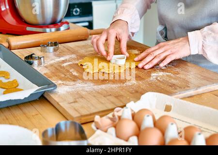 Die Hände der Frau schneiden Kekse in Form eines Herzens auf dem Tisch der Küche aus. Hausgemachtes Gebäck oder Kuchen. Kekse backen. Stockfoto